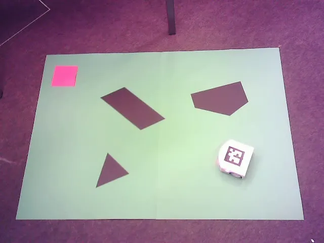 Overhead view of the Thymio robot with an ArUco marker on a green arena with dark obstacles and a pink goal